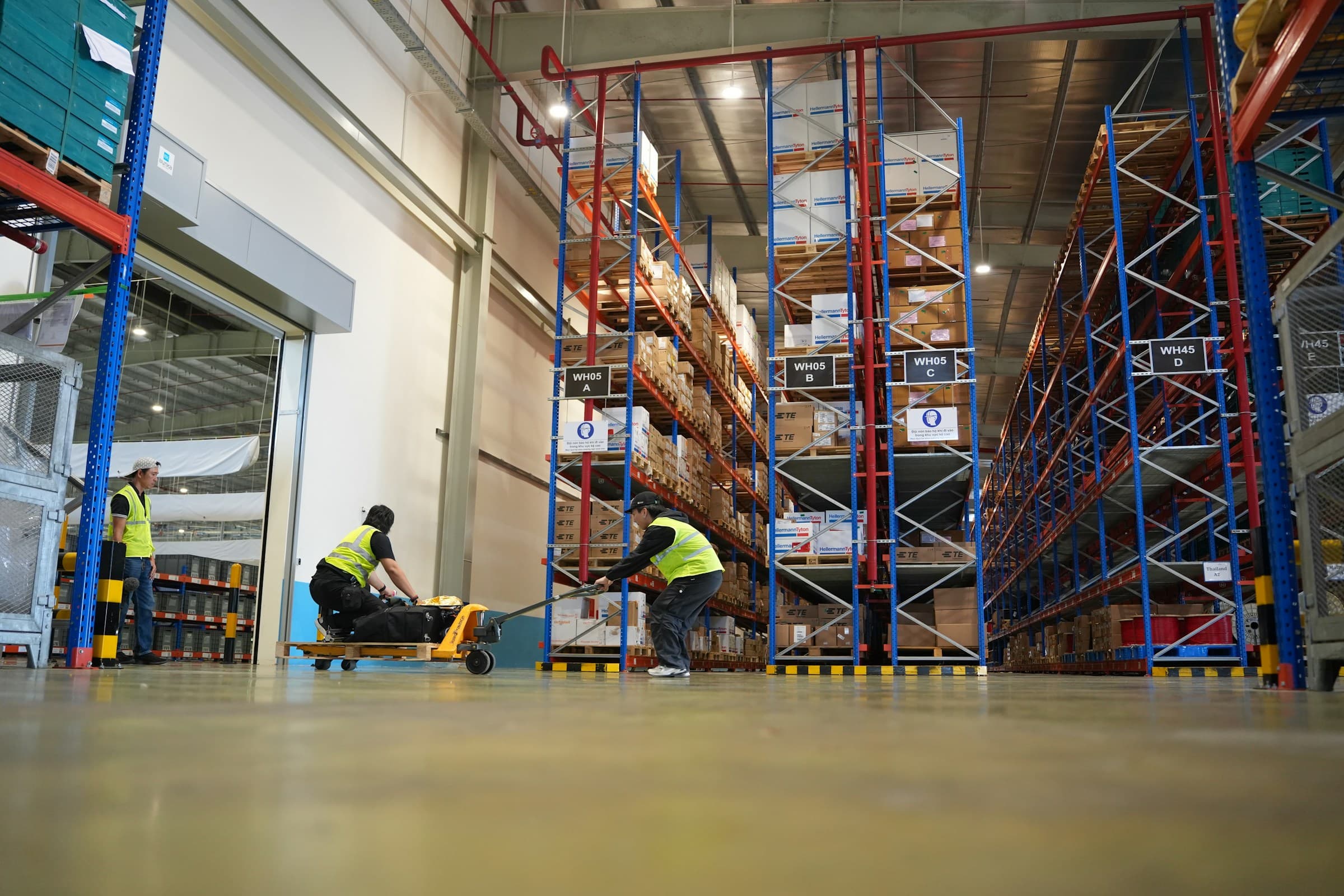Warehouse associates moving palletized inventory through aisles of high-bay industrial racking.