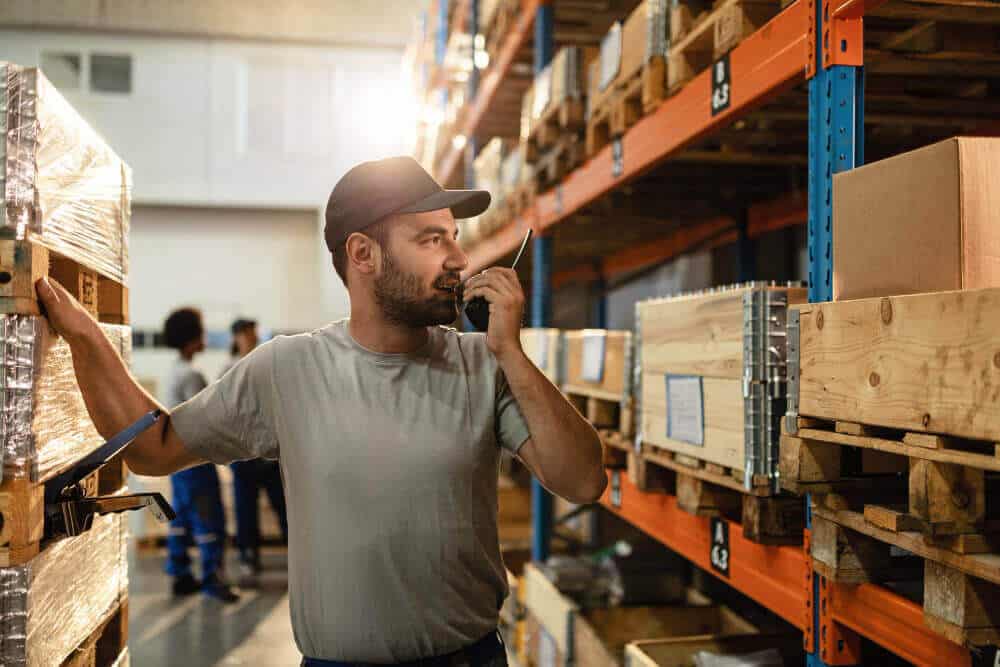 Male Warehouse Worker Communicating With Someone Walkietalkie While Standing Among Shelfs Distribution Warehouse