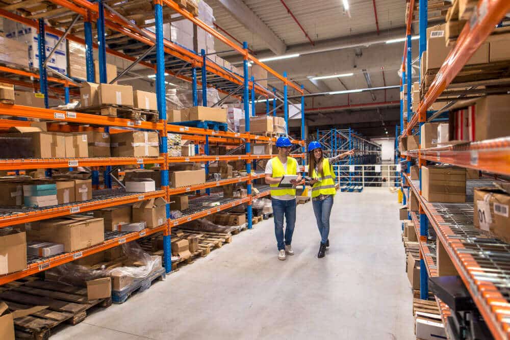 Two Warehouse Workers Walking Distribution Storage Area Discussing About Logistics Organization
